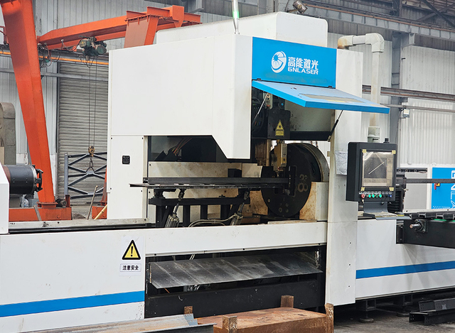 Modern bridge manufacturing equipment with a worker operating a large steel beam cutting machine.